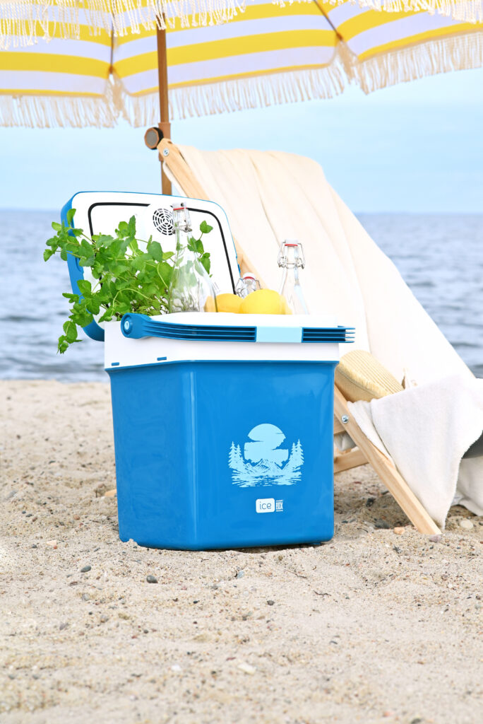 Niebieska lodówka turystyczna na plaży z napojami, cytrynami i miętą
