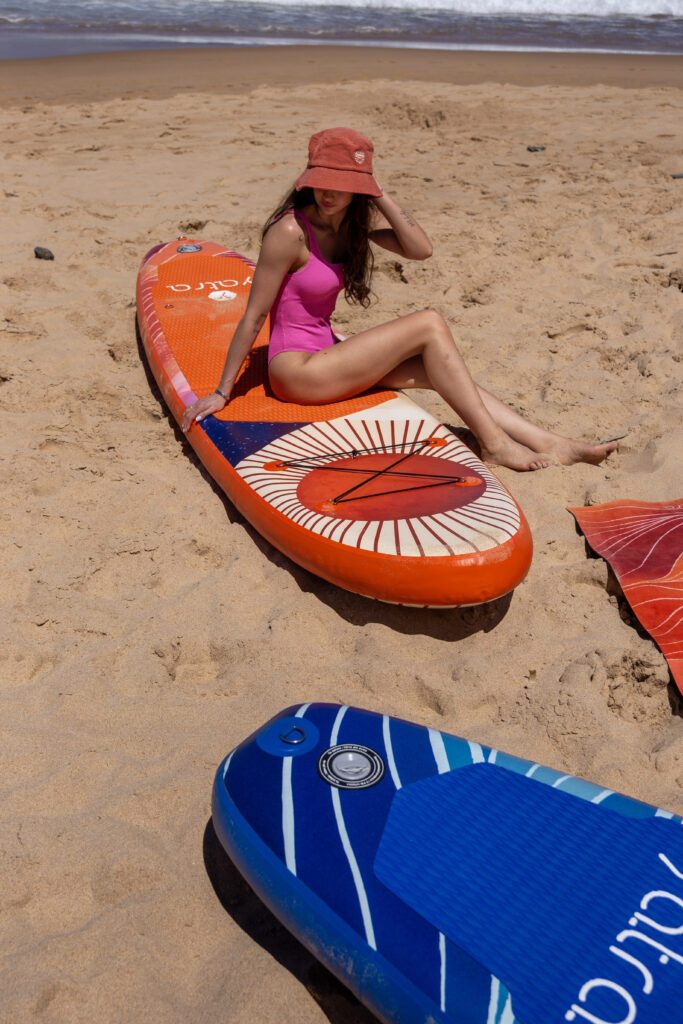 Kobieta siedząca na dmuchanej desce SUP Yatra na piaszczystej plaży przed rozpoczęciem pływania.